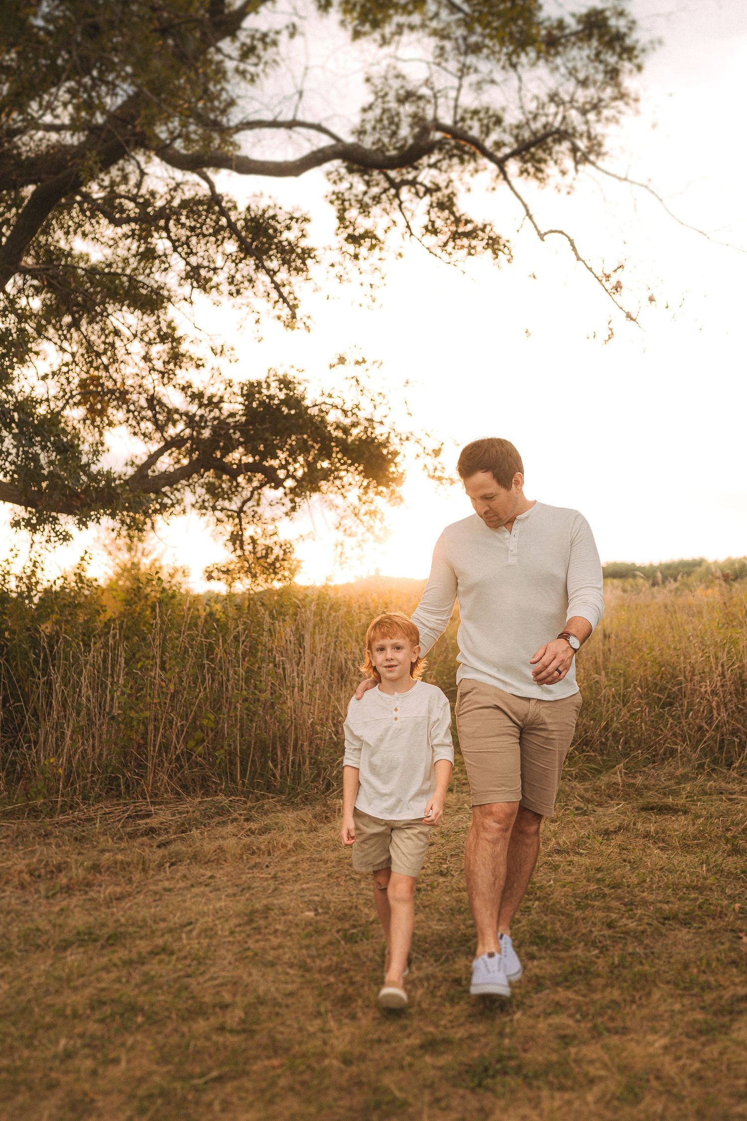 Two people walking together at sunset under a large tree branch.