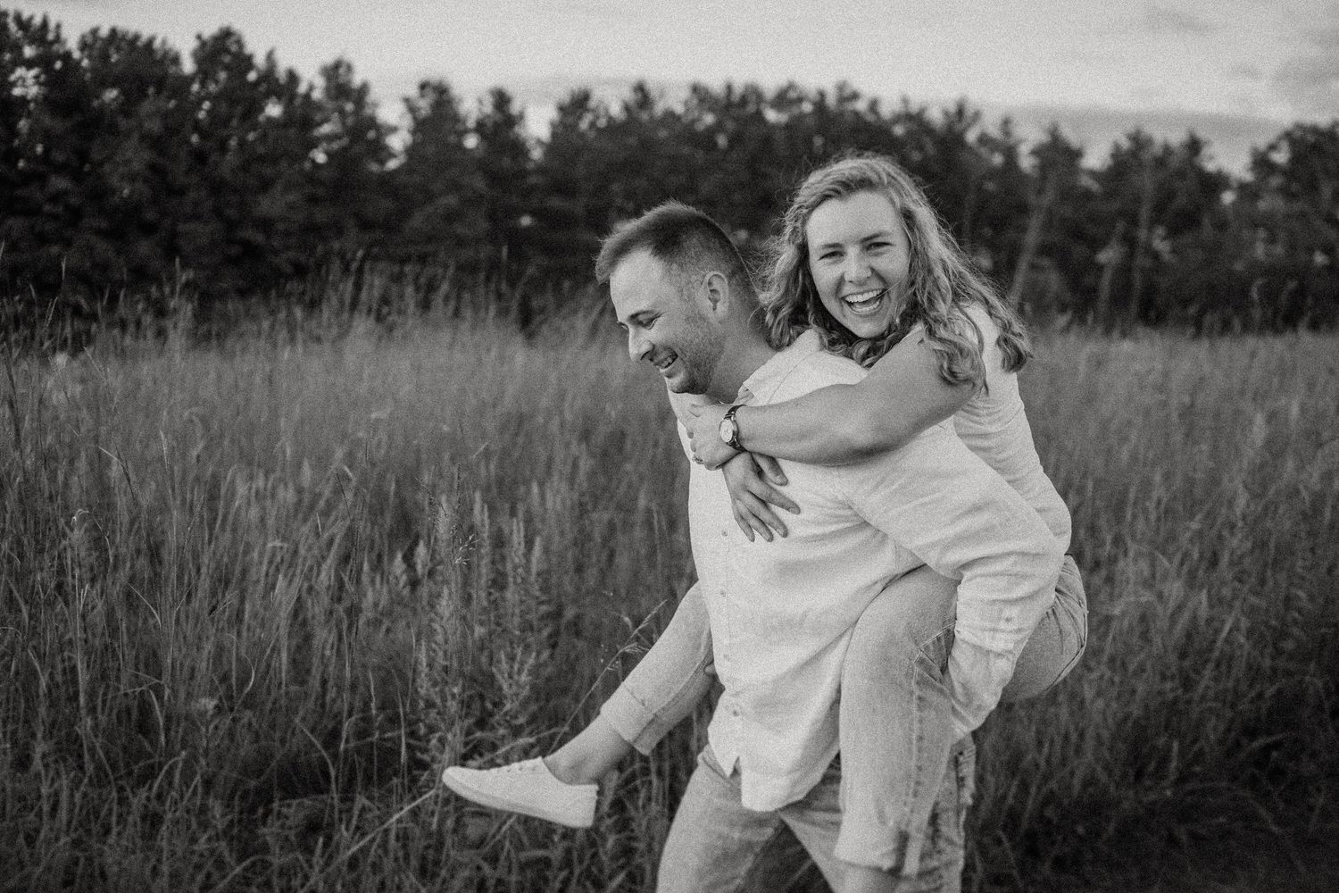 Black and white photo of joyful piggyback ride in grassy meadow.