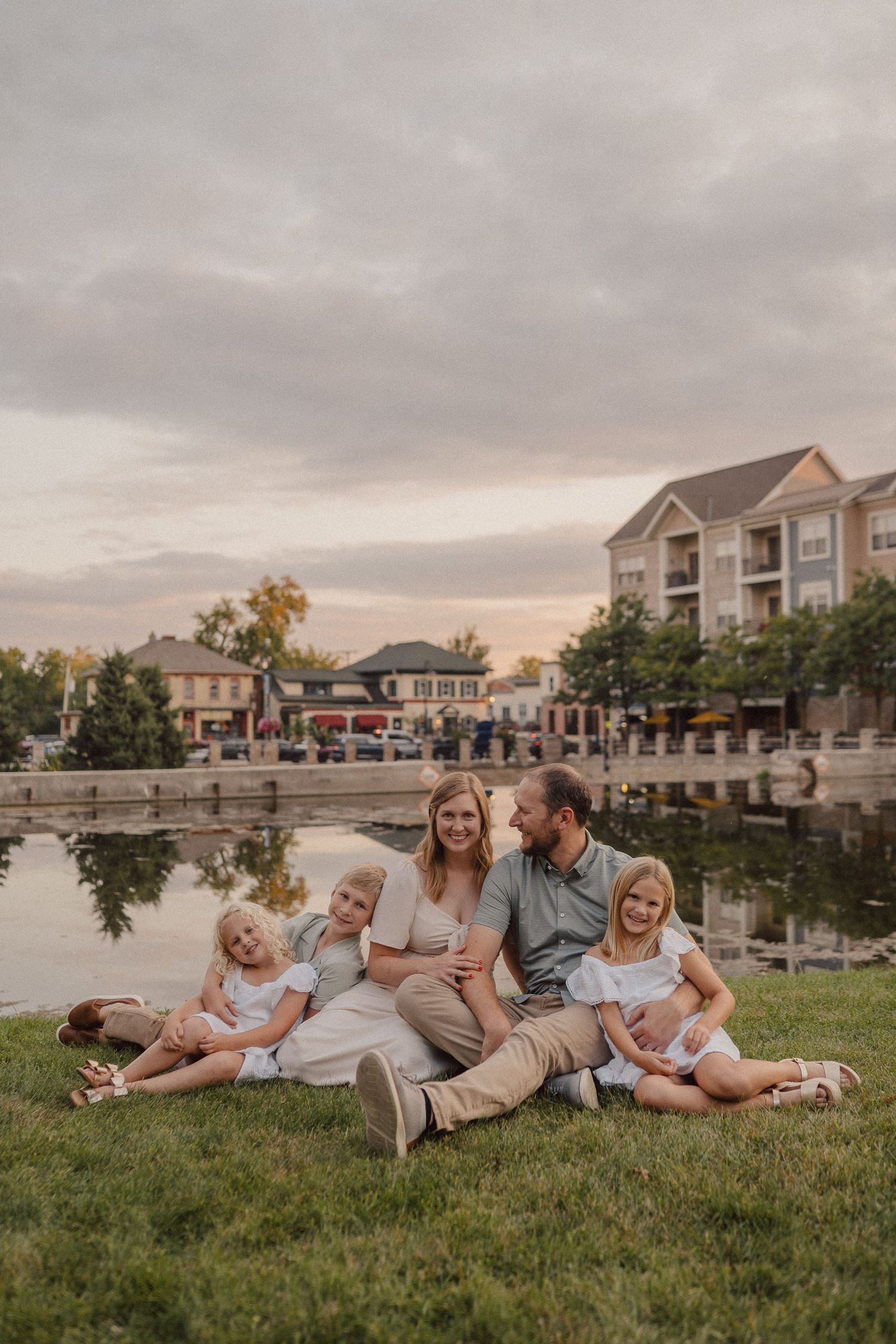 A family lying together on grass at sunset with residential townhomes in the background.