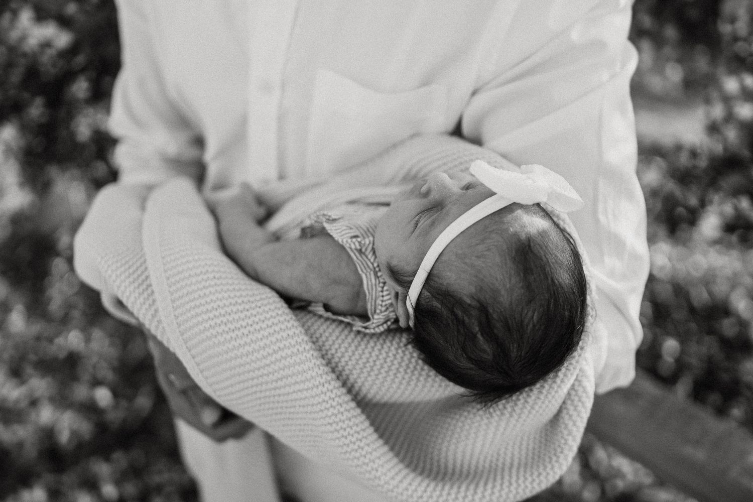 A tender black and white photograph of a newborn baby being cradled in a caregiver's arms.