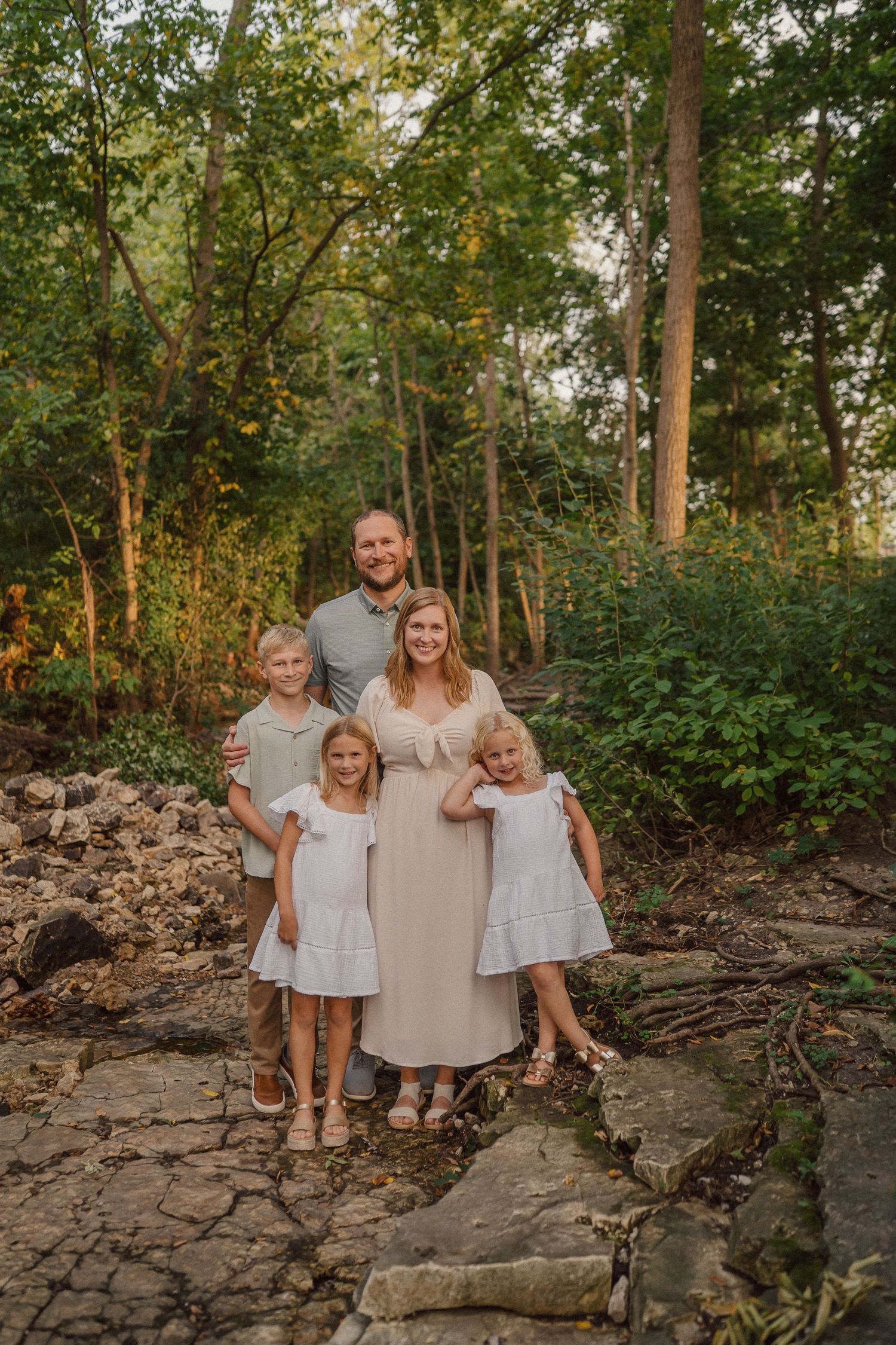 Family standing together on rocky terrain with trees and greenery in the background.