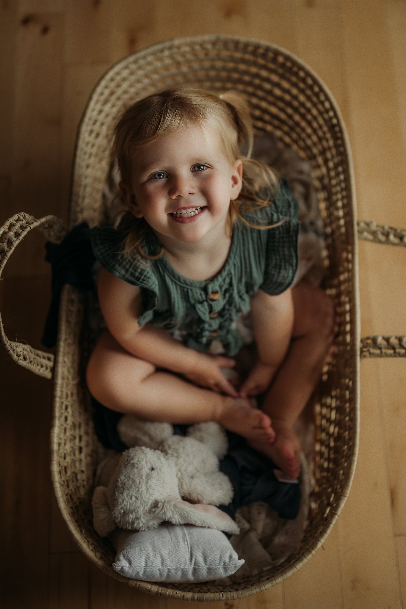 Happy toddler sitting in woven basket chair with stuffed animal.