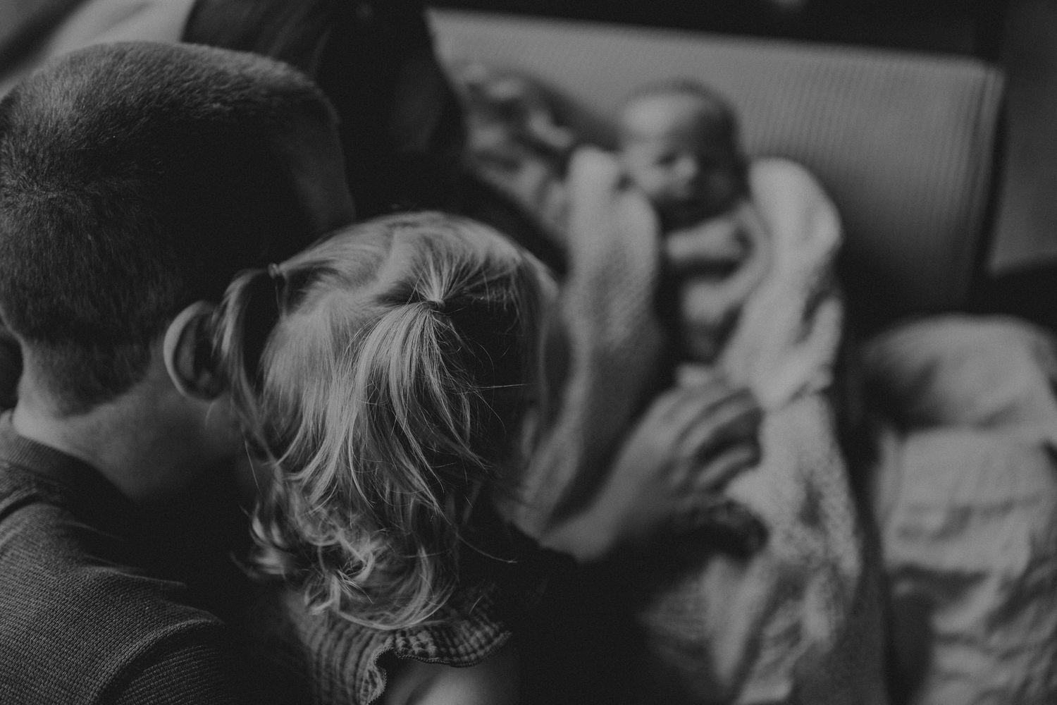 Black and white image of a family moment on a couch with soft window light.