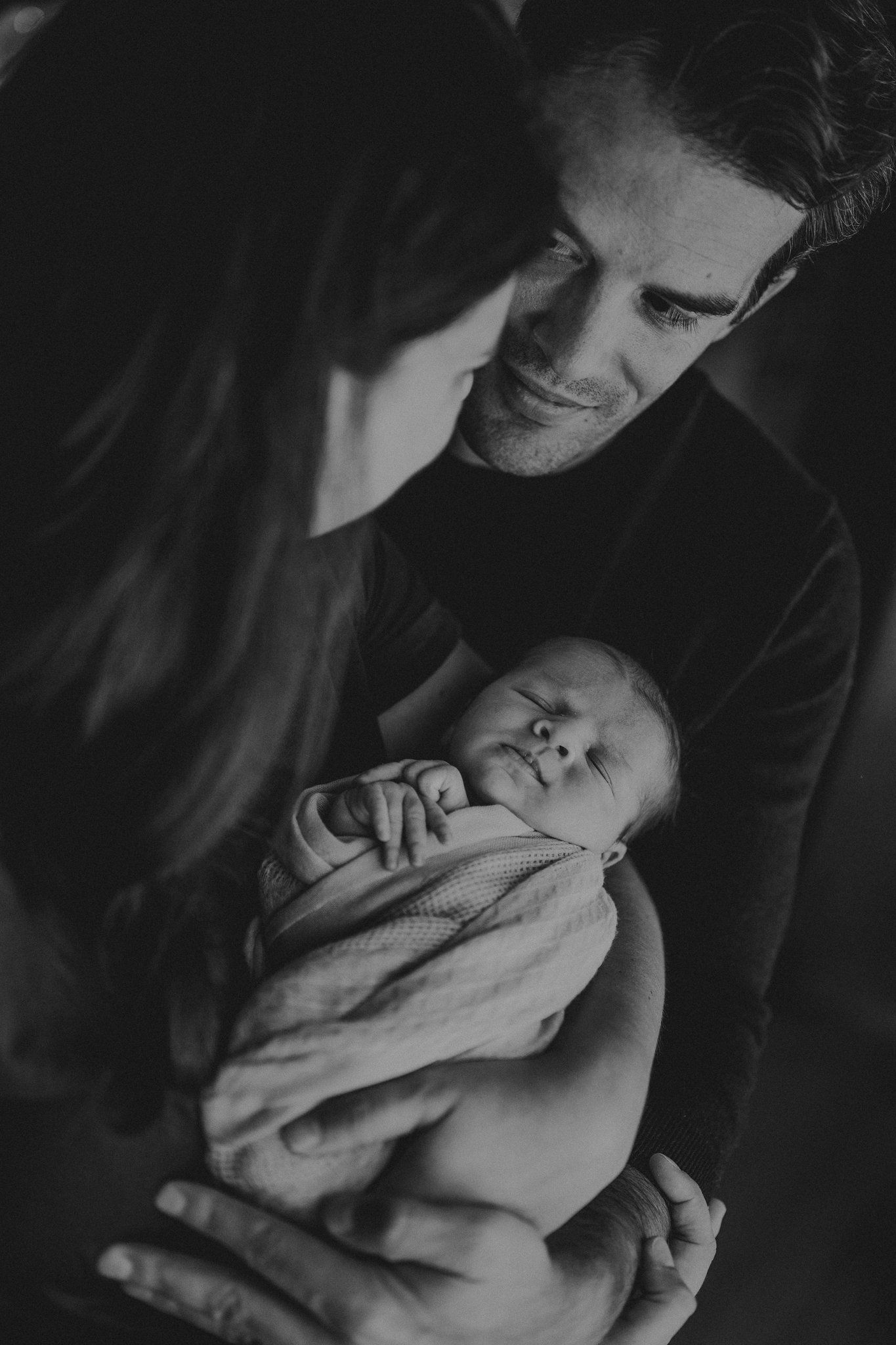 Black and white portrait of newborn being cradled in soft blanket.