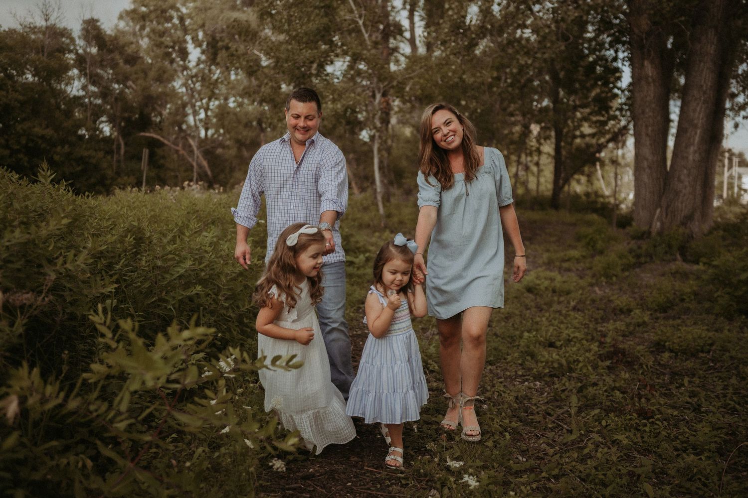 Natural family photo walking together through a grassy woodland path.