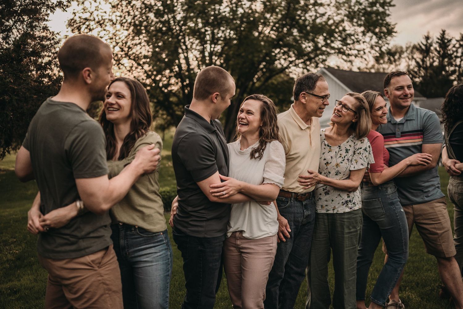 Couples share intimate moments and laughter while standing together in a park at sunset.