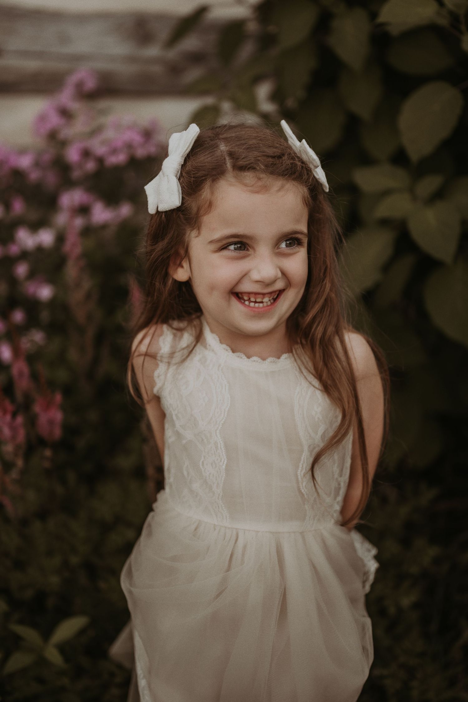 White dress with lace detail shown against garden with pink flowering bushes.
