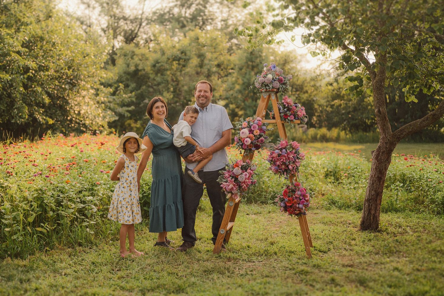 Family photoshoot in natural outdoor setting with decorative floral ladder and evening light.
