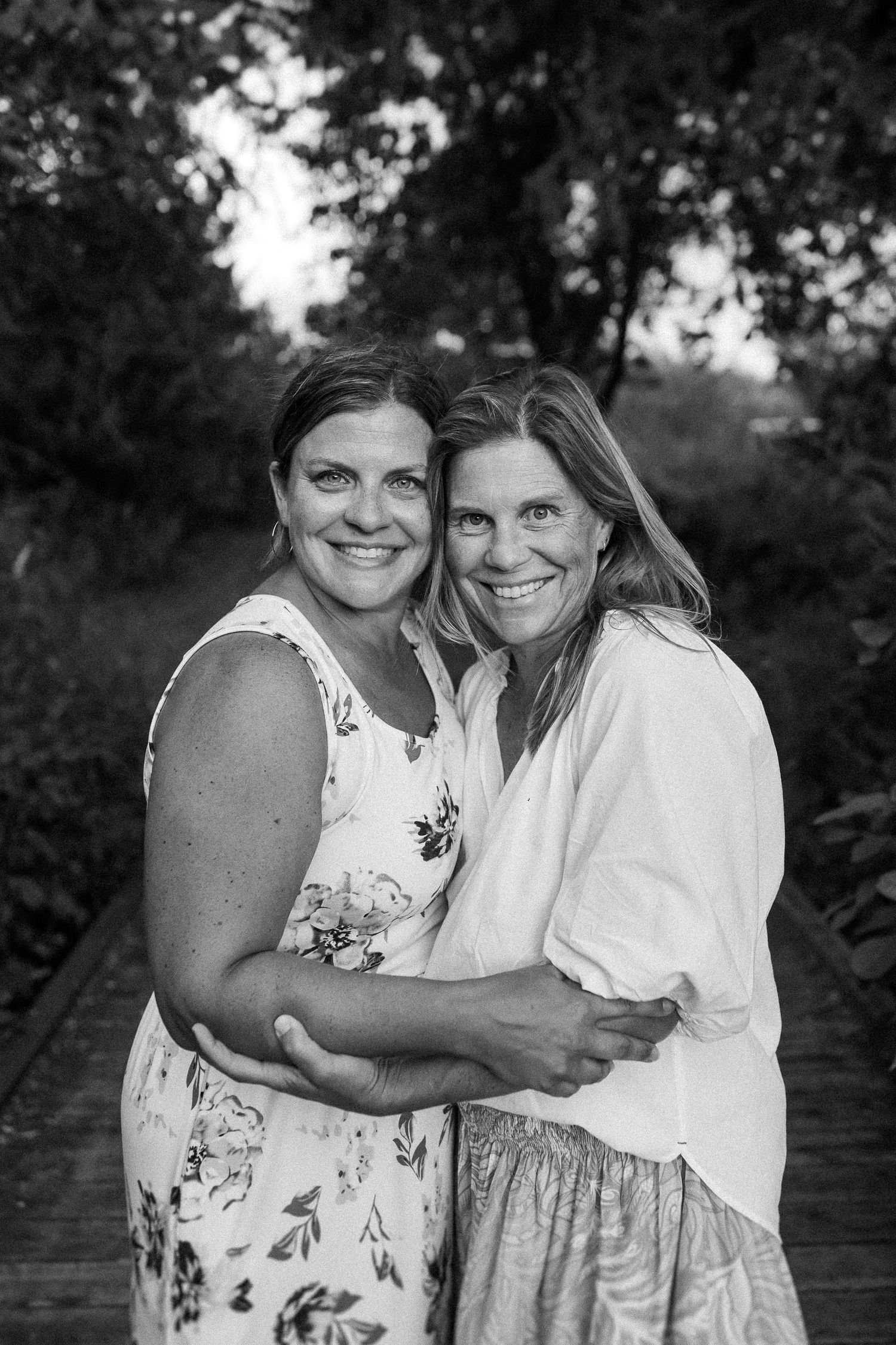 Two people embrace and smile in a black and white outdoor portrait with natural lighting.
