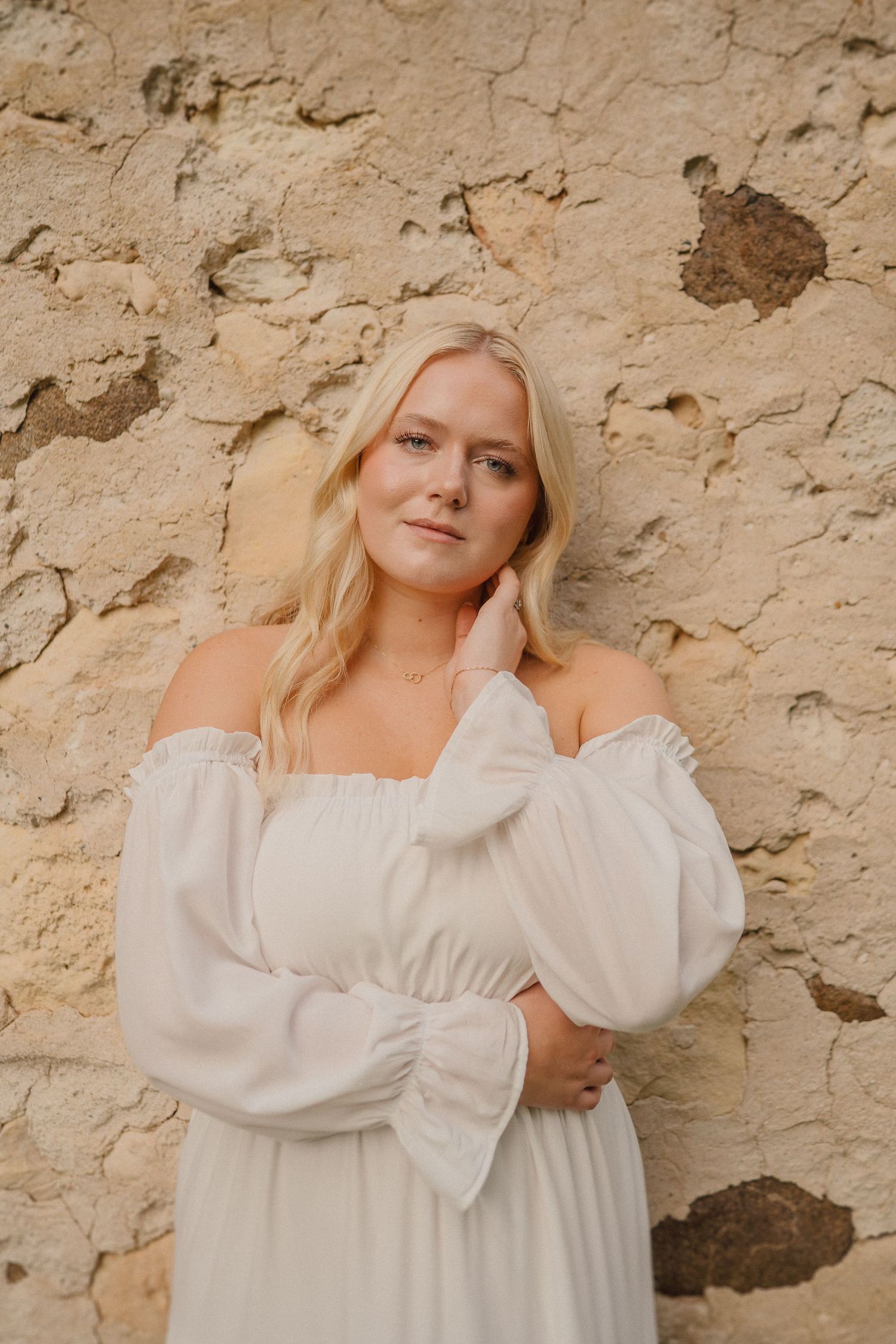 White peasant dress photographed against textured stone wall with natural lighting.