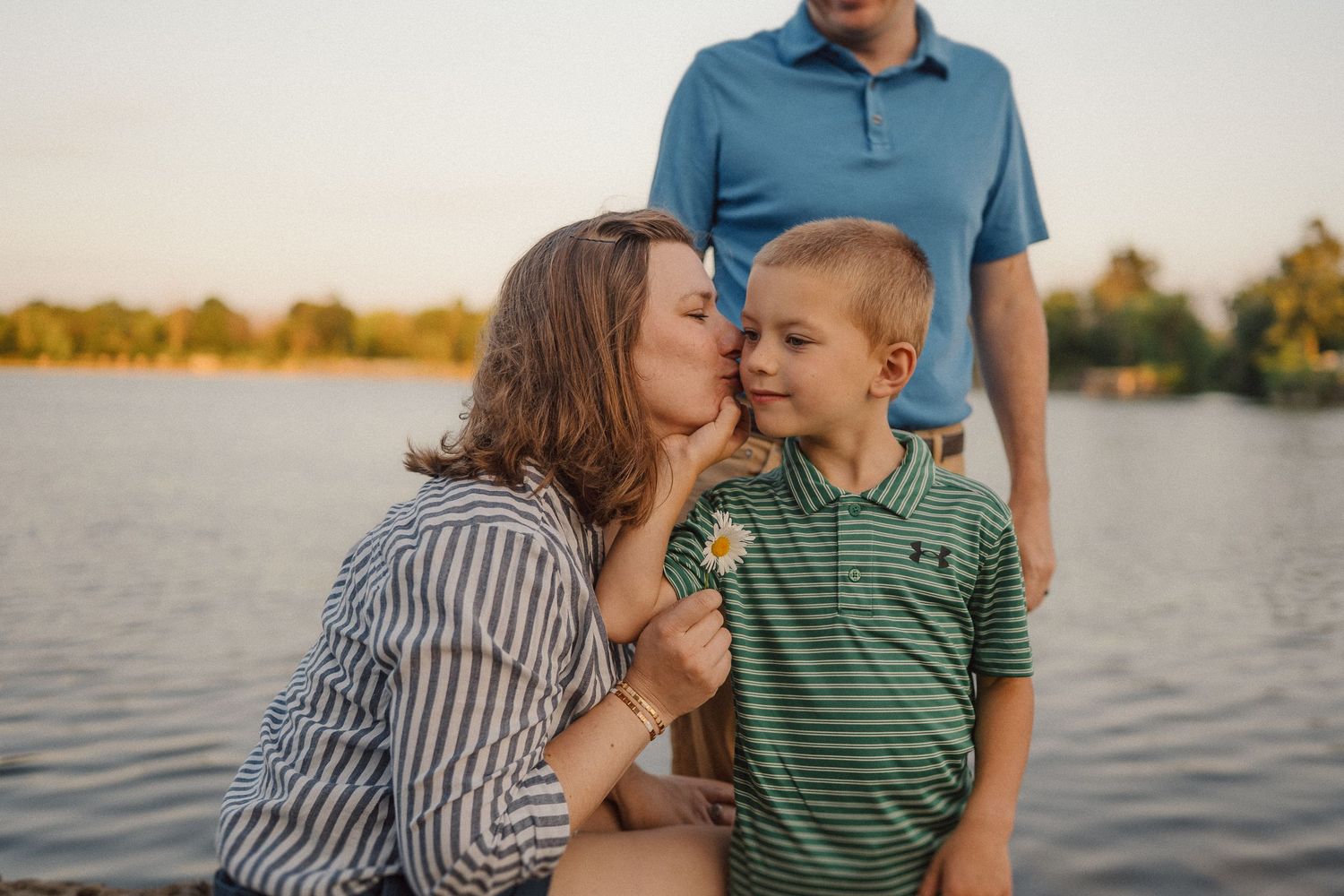 A loving family moment captured by the water during sunset with soft golden light.