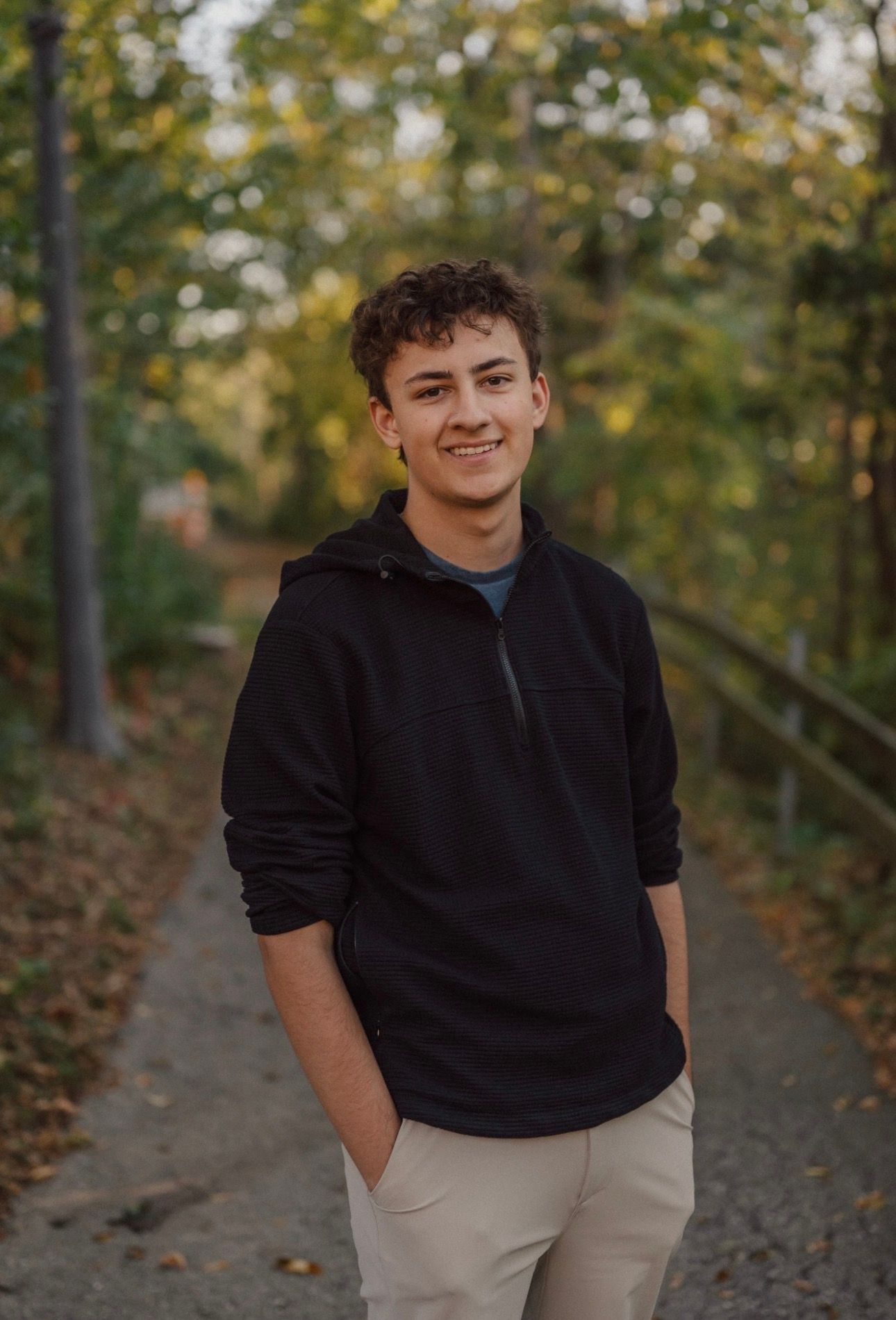 Casual outdoor portrait in autumn setting wearing black hoodie and khaki pants on wooded path.
