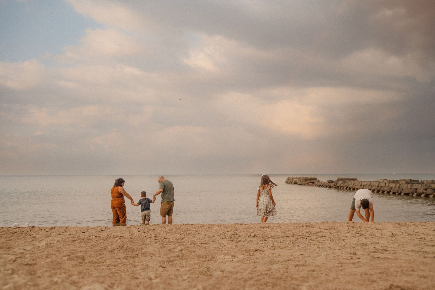 Silhouettes of people enjoying time together on a beach at dusk with cloudy skies above.