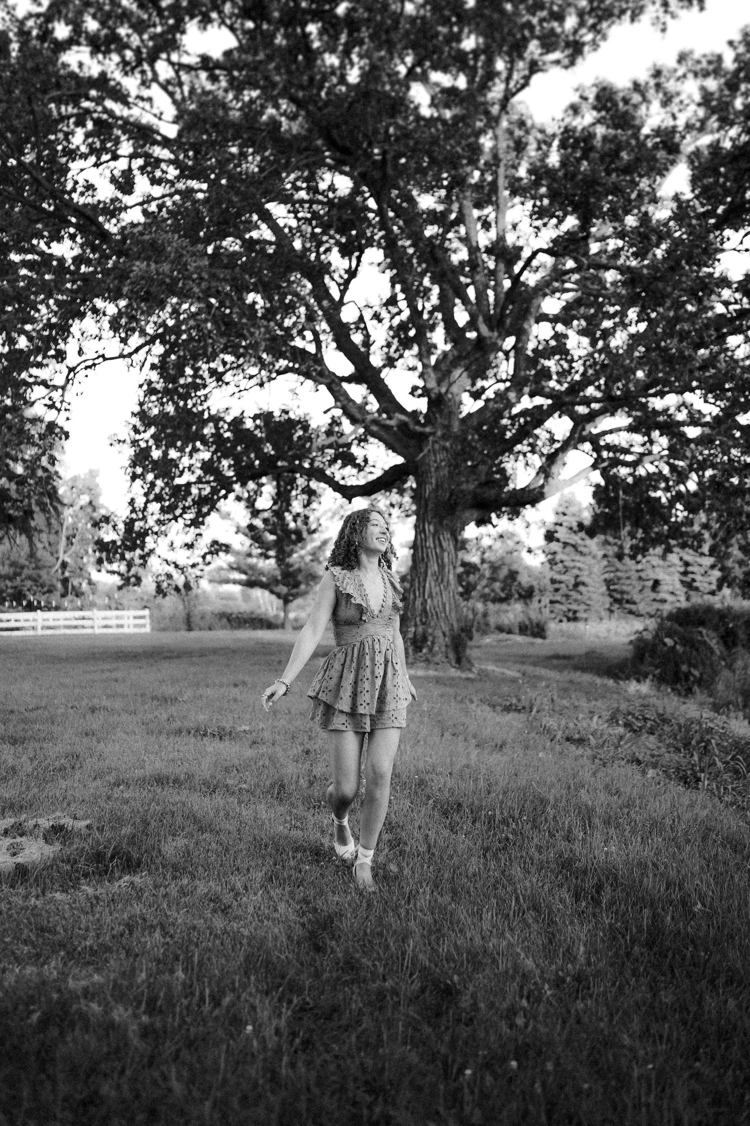 Black and white scene of children playing and running on a grassy hillside under oak trees.