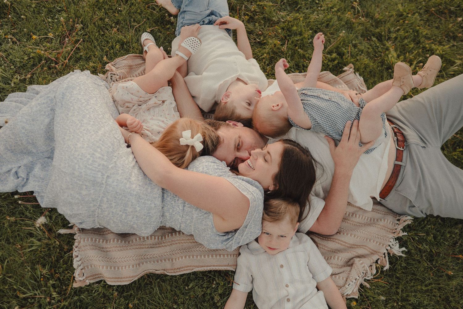 Family of four lying on a blanket in the grass sharing a tender moment together.