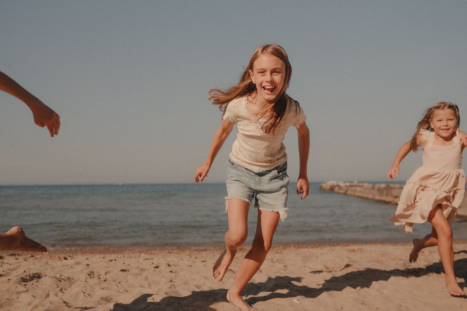 Happy children running barefoot on sandy beach on a sunny day with ocean waves in background.