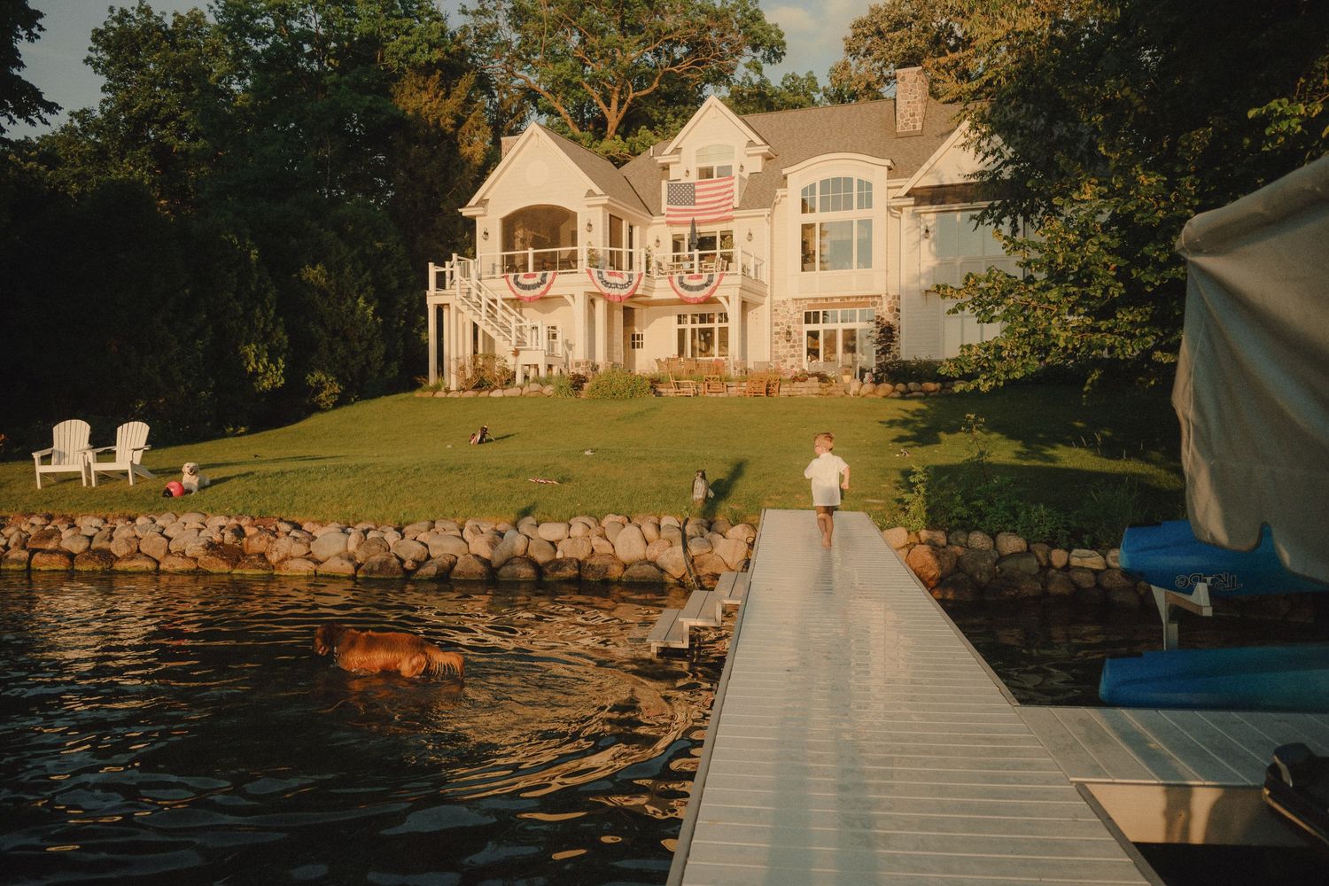 A person walks along a dock toward a large lakeside home at golden hour.
