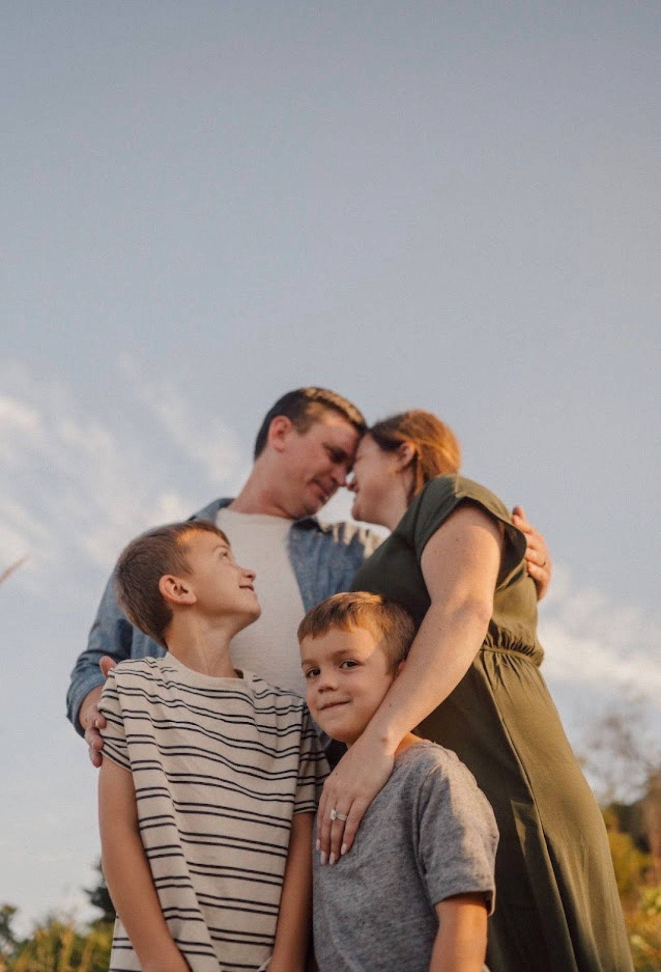 A tender family moment captured against a blue sky during golden hour.