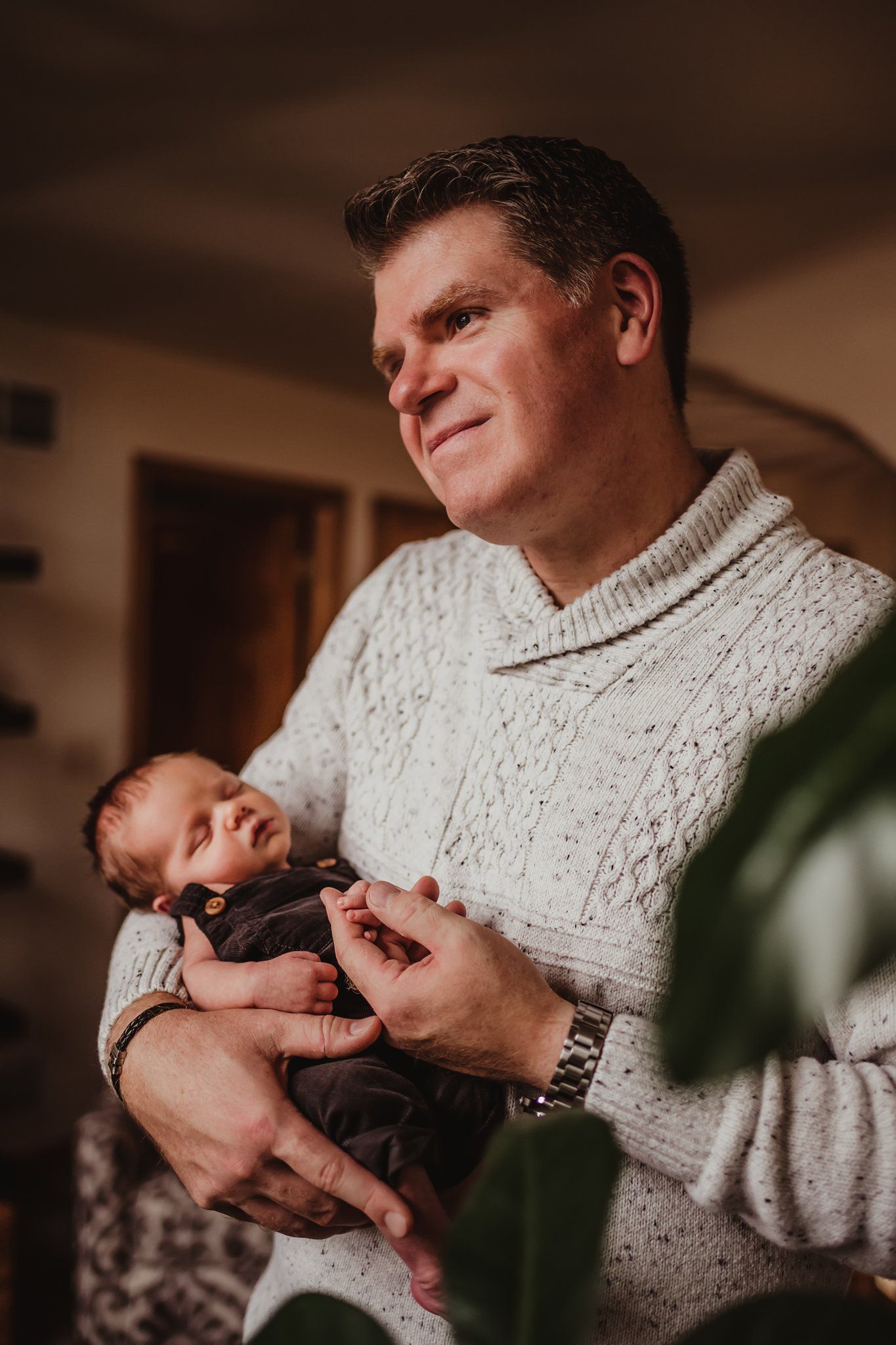 A heartwarming indoor portrait of a parent wearing a cream sweater while cradling a sleeping newborn.