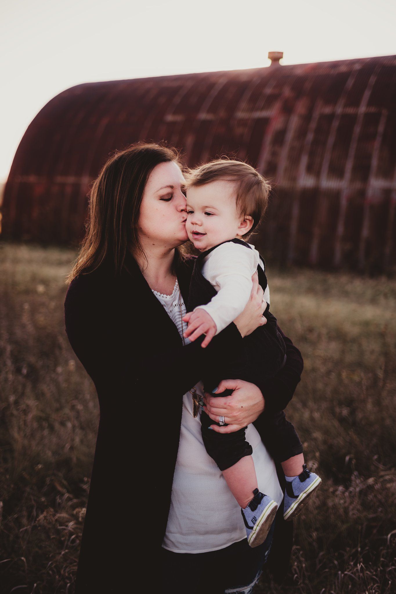 Tender moment captured between parent and child against rustic barn backdrop at sunset.