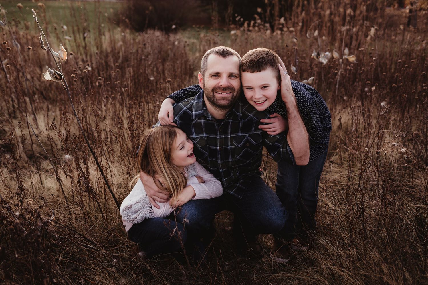 A loving family moment captured in golden hour light among tall grasses.