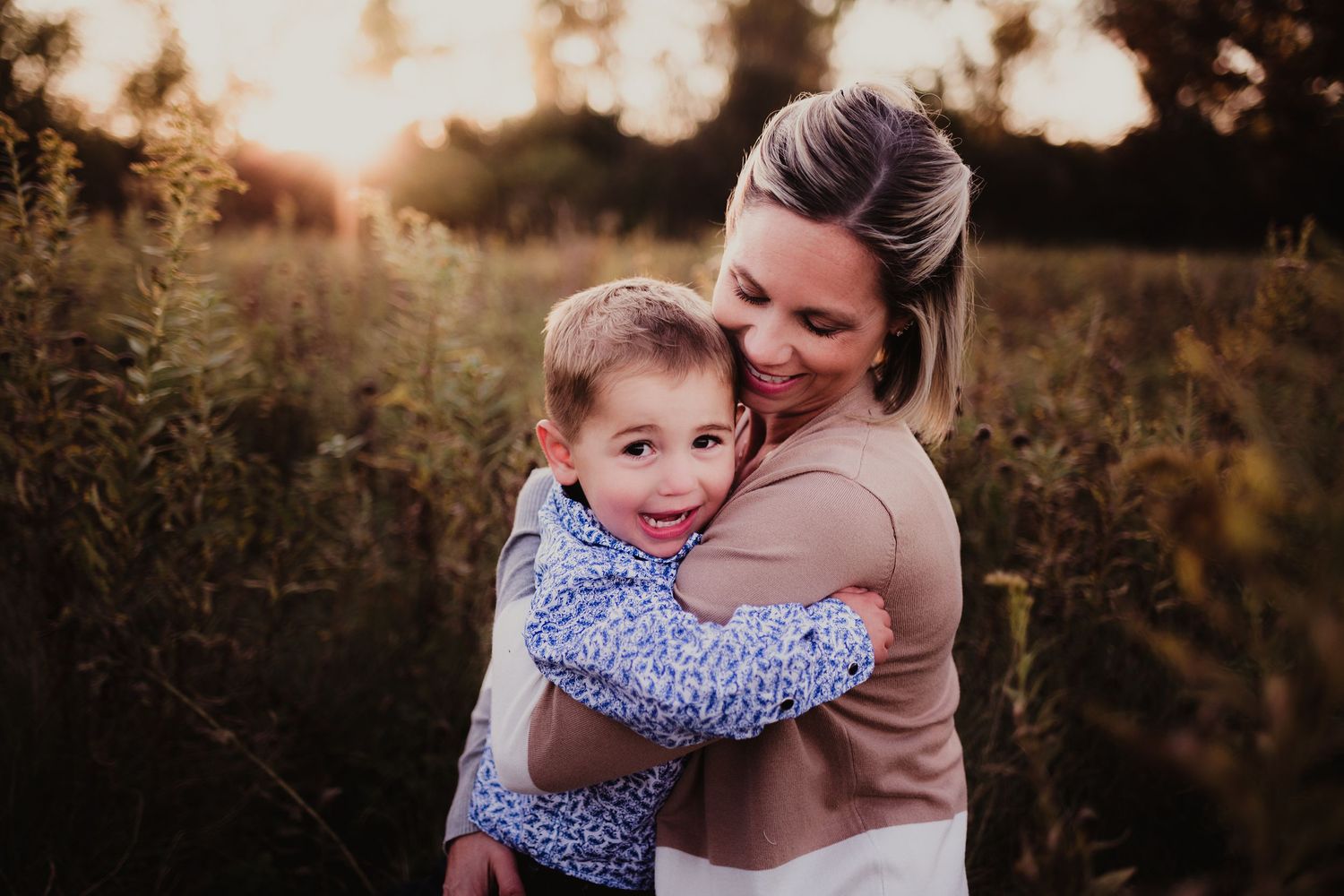 Tender outdoor portrait of parent and child embracing at sunset in golden field.