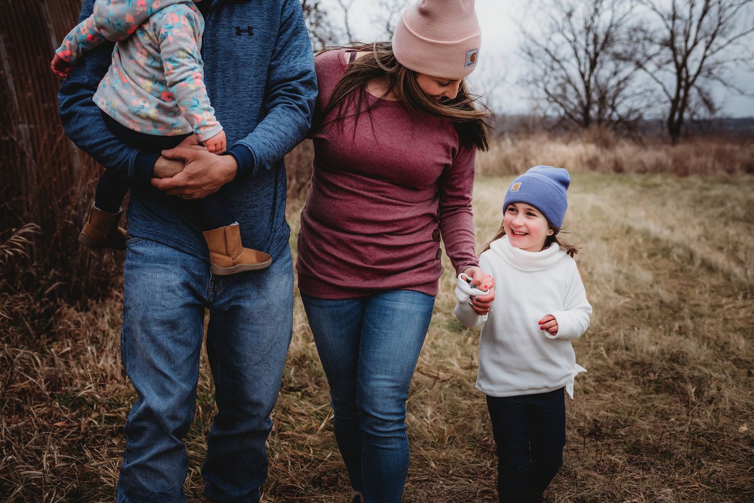 Casual winter family photo showing walking poses against rustic barn backdrop.