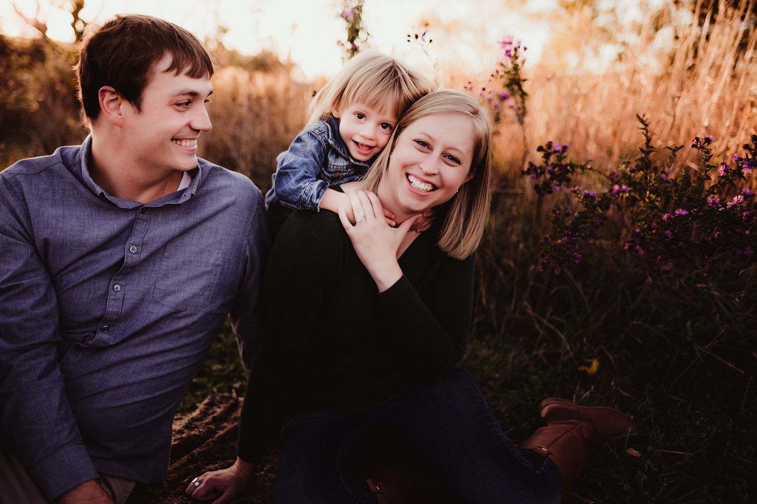 Three people pose together outdoors during golden hour in a natural setting.