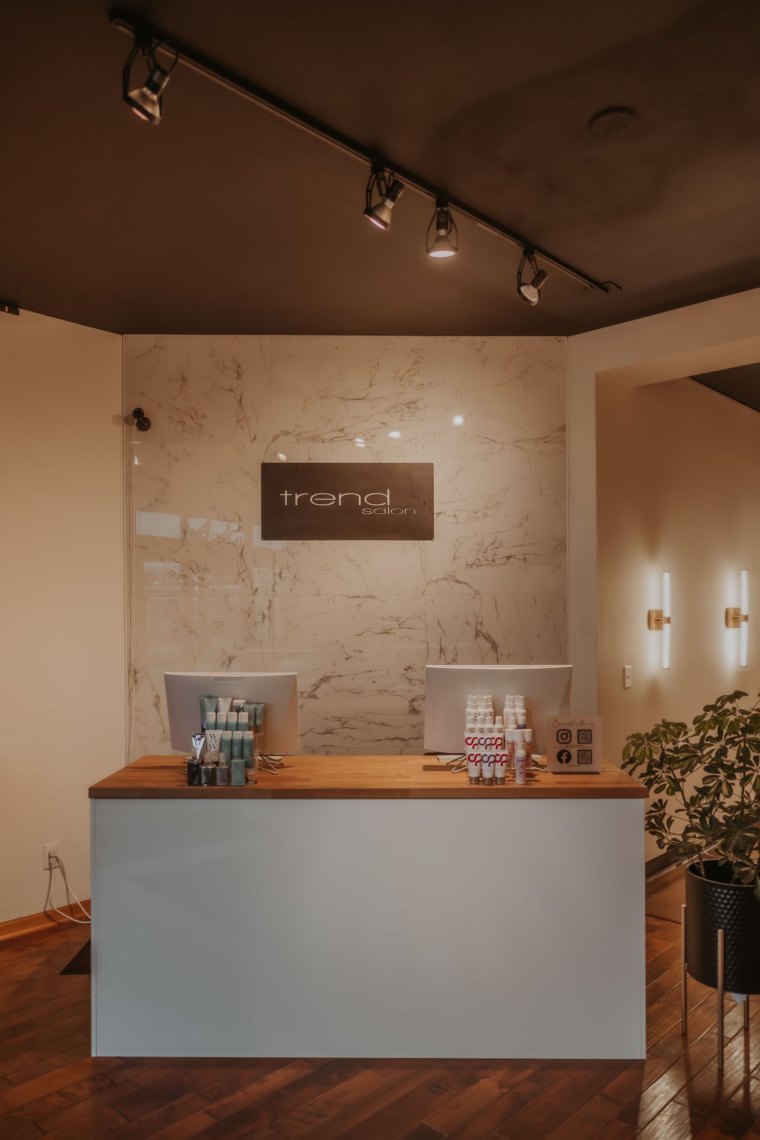 Modern salon reception desk with wooden counter and track lighting under trendy branding signage.