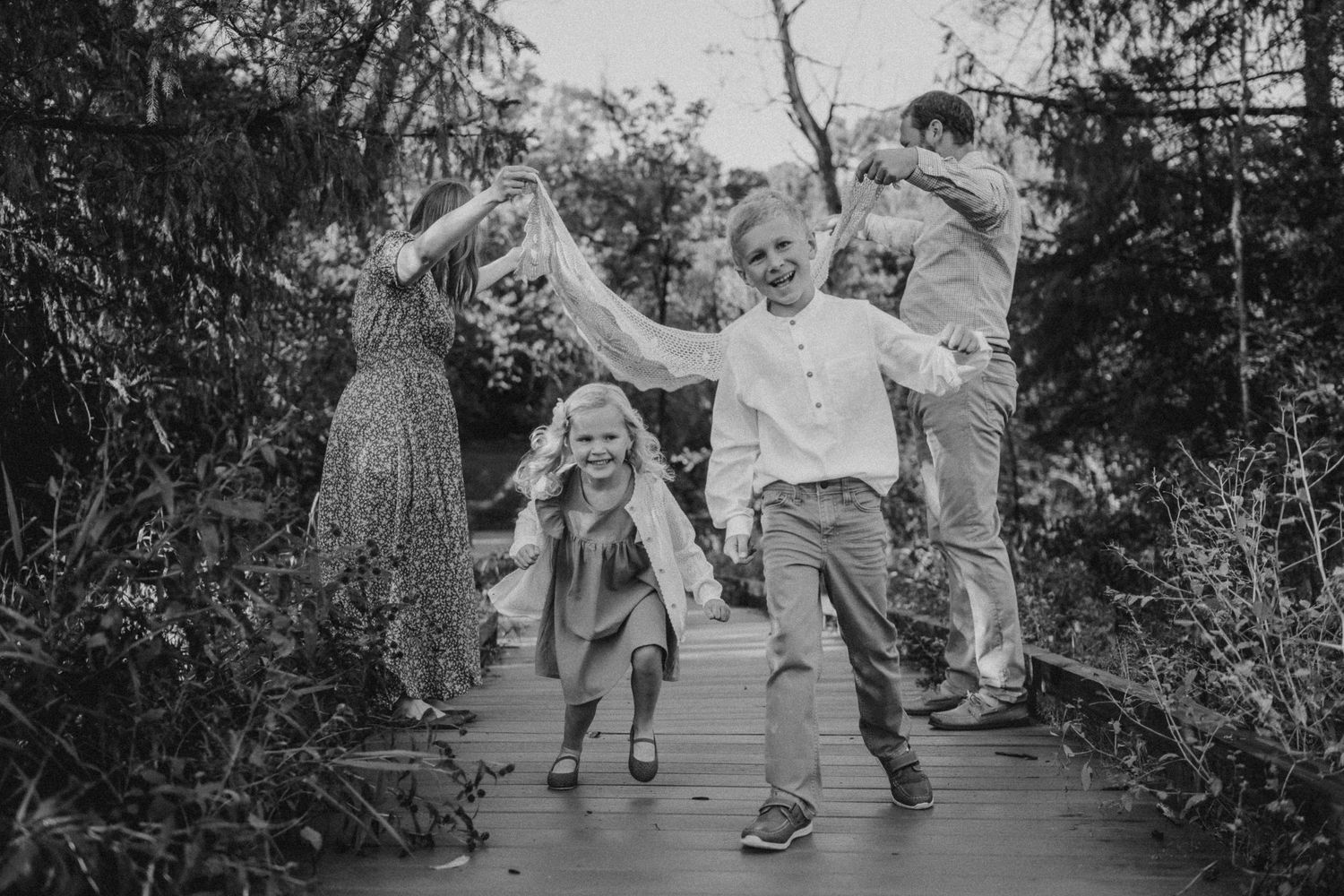 A candid black and white photo of people dancing and jumping on a wooden boardwalk.