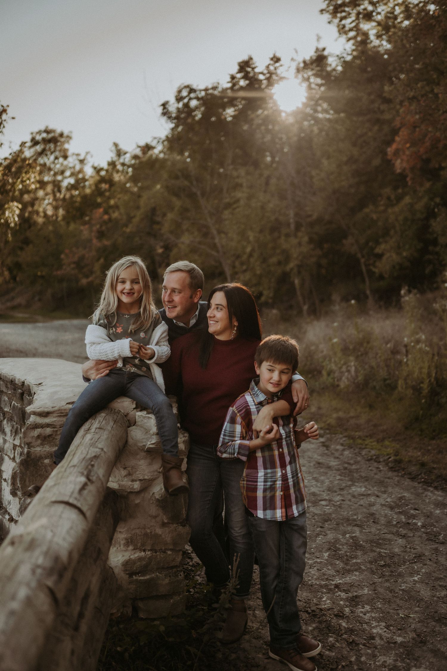 Family shares intimate moment together on wooden fence during sunset in wooded setting.