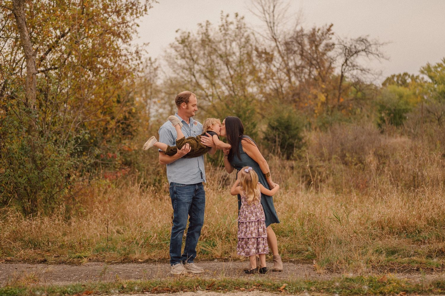 A heartwarming outdoor family moment captured against a backdrop of fall trees and golden light.