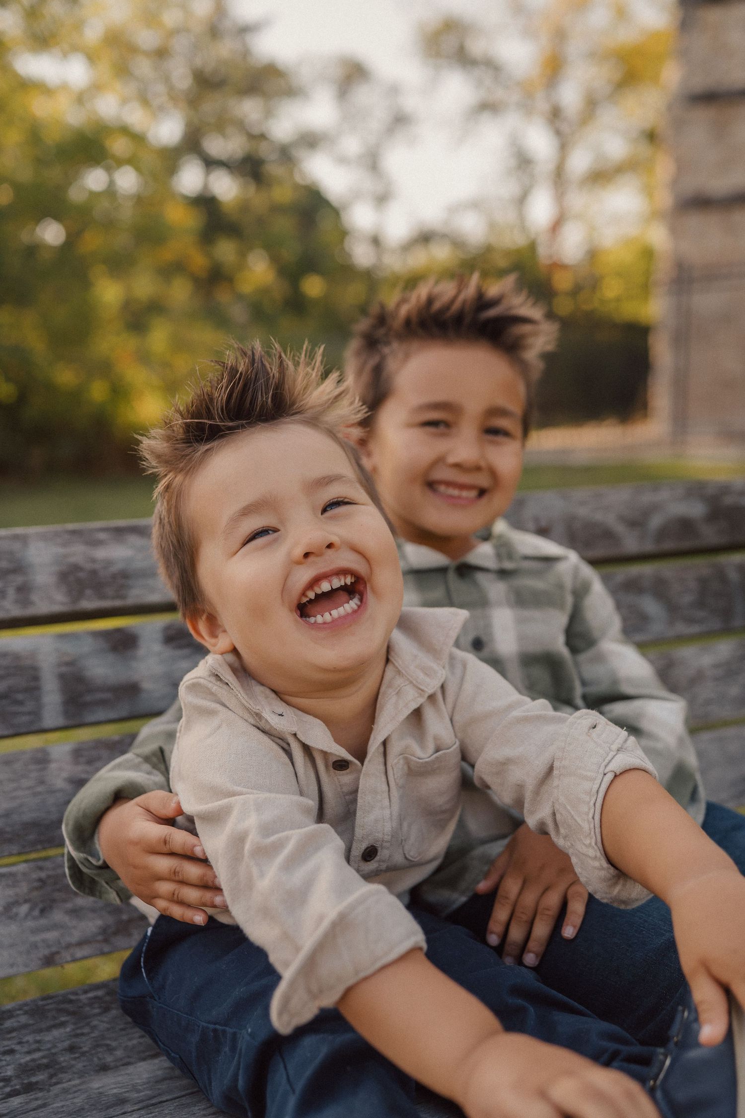 Two children share infectious laughter while sitting close together on a wooden bench.