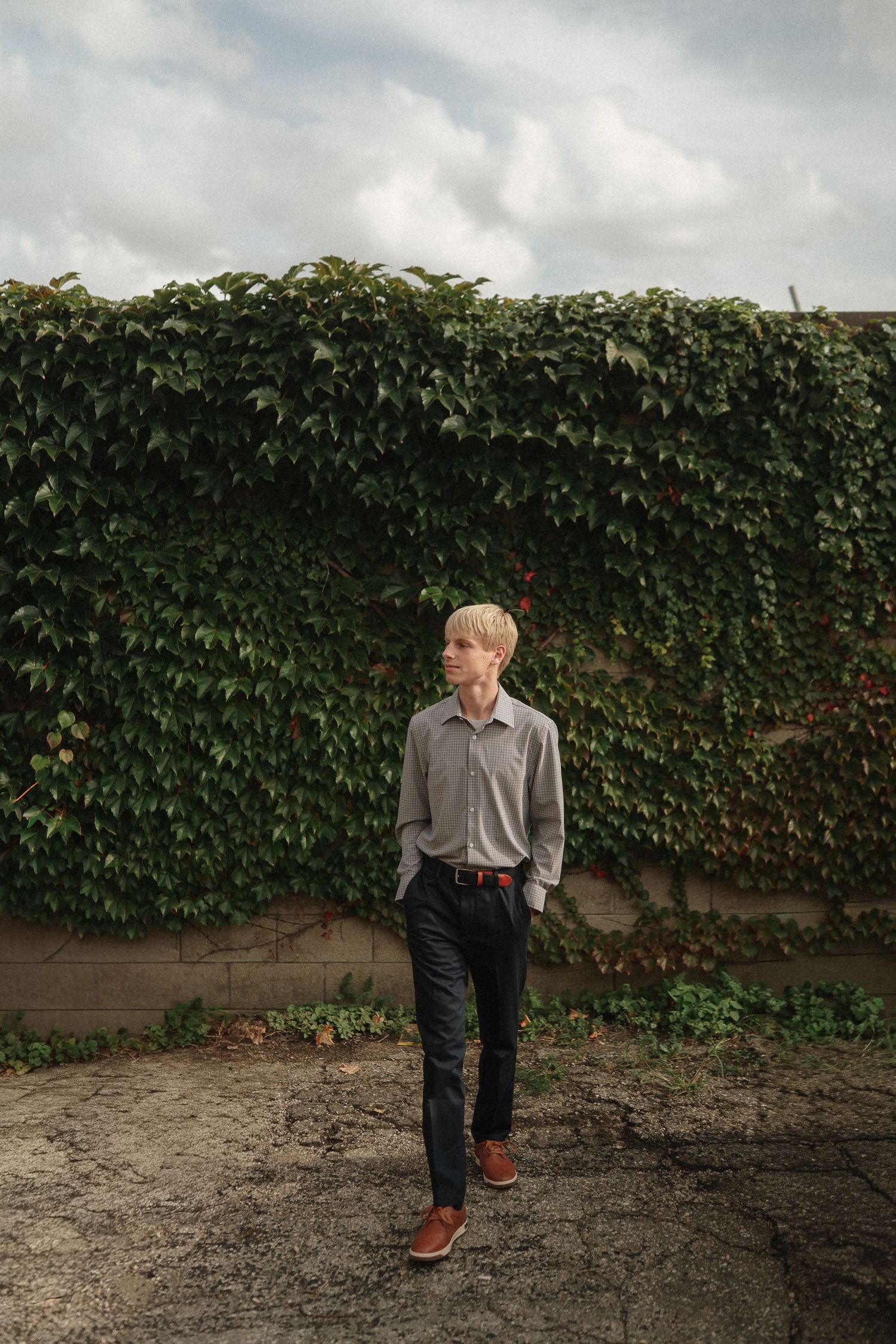 A figure walking across dirt ground against an ivy-covered wall backdrop on an overcast day.