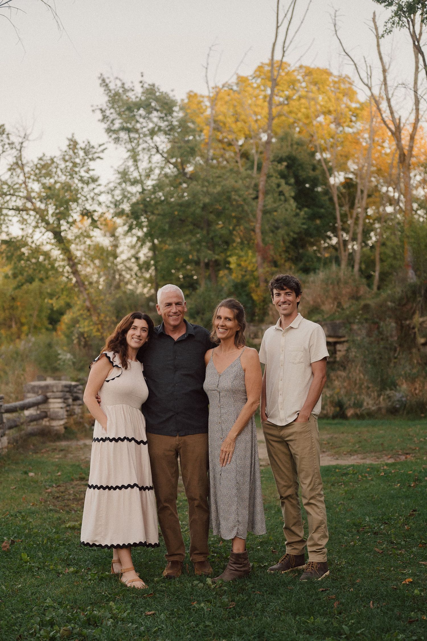 A group stands together outdoors in casual attire against a backdrop of autumn trees with golden foliage.