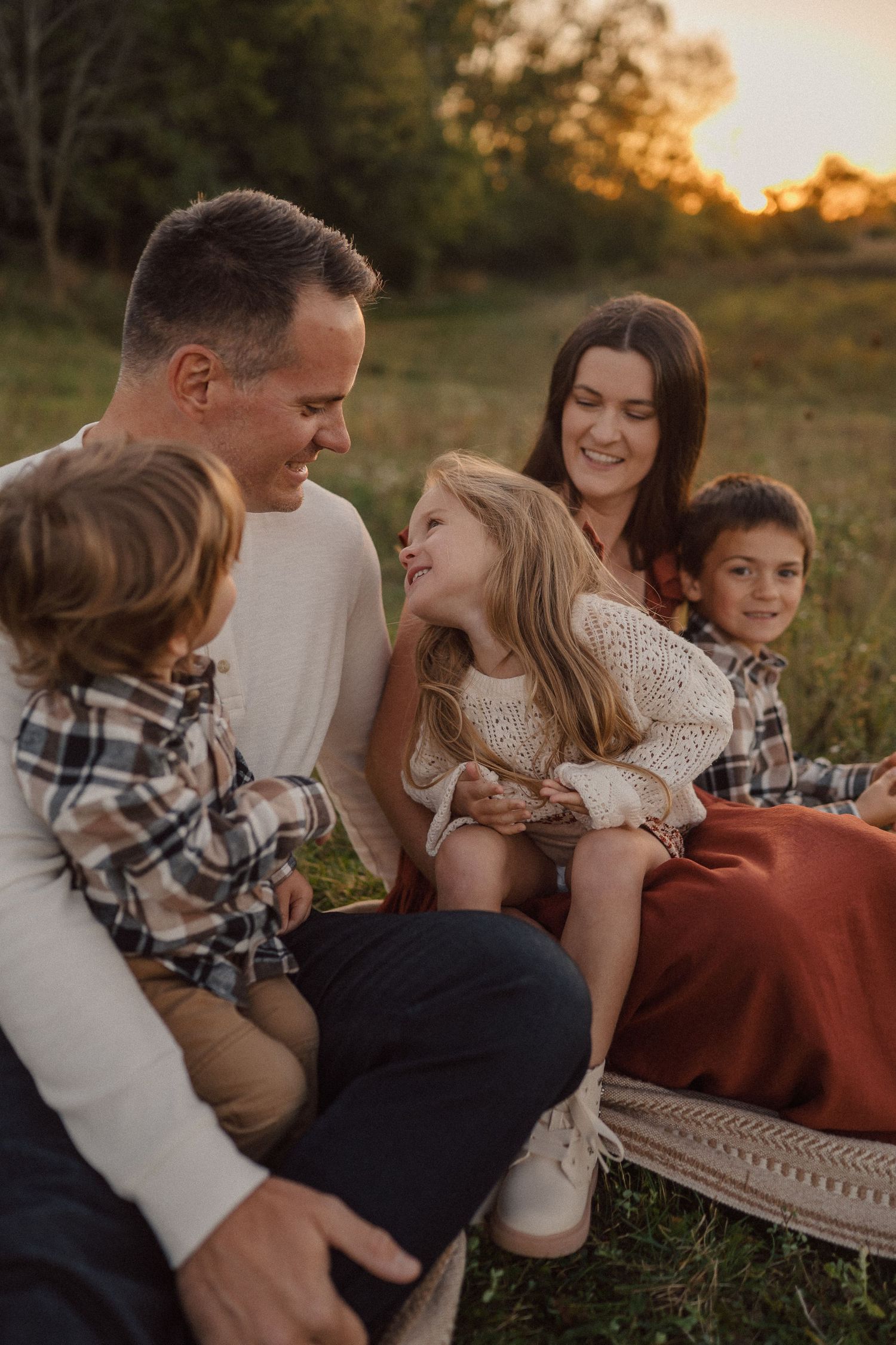 Family enjoying playful moments together on grass during golden hour with coordinated outfits.