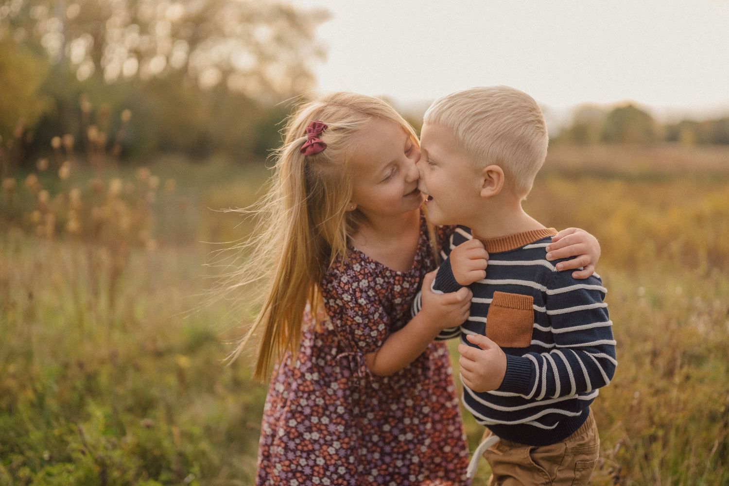 Two young children play together in a golden autumn field at sunset.
