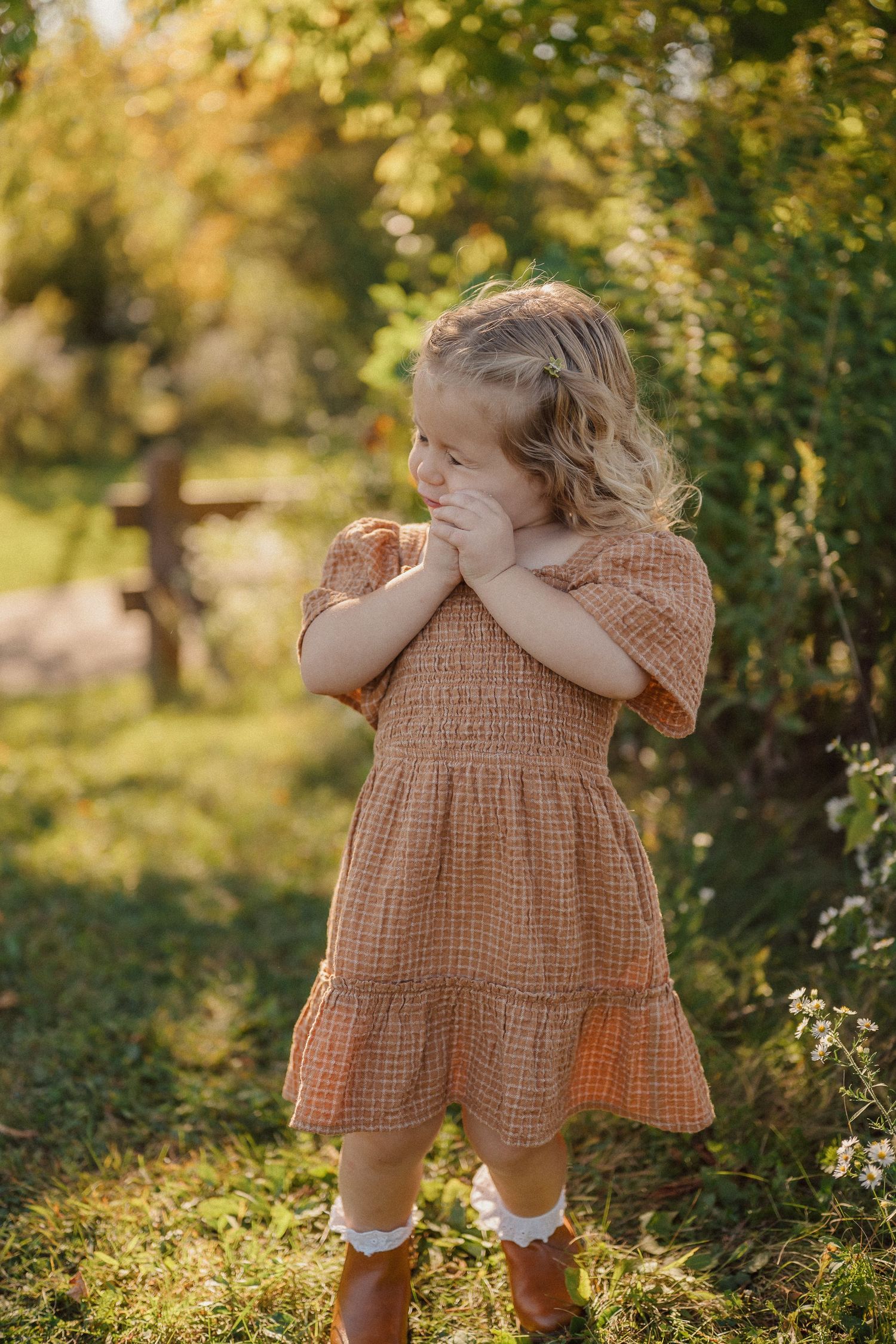 A playful moment captured in a garden as a child in a brown dress dances among the greenery.