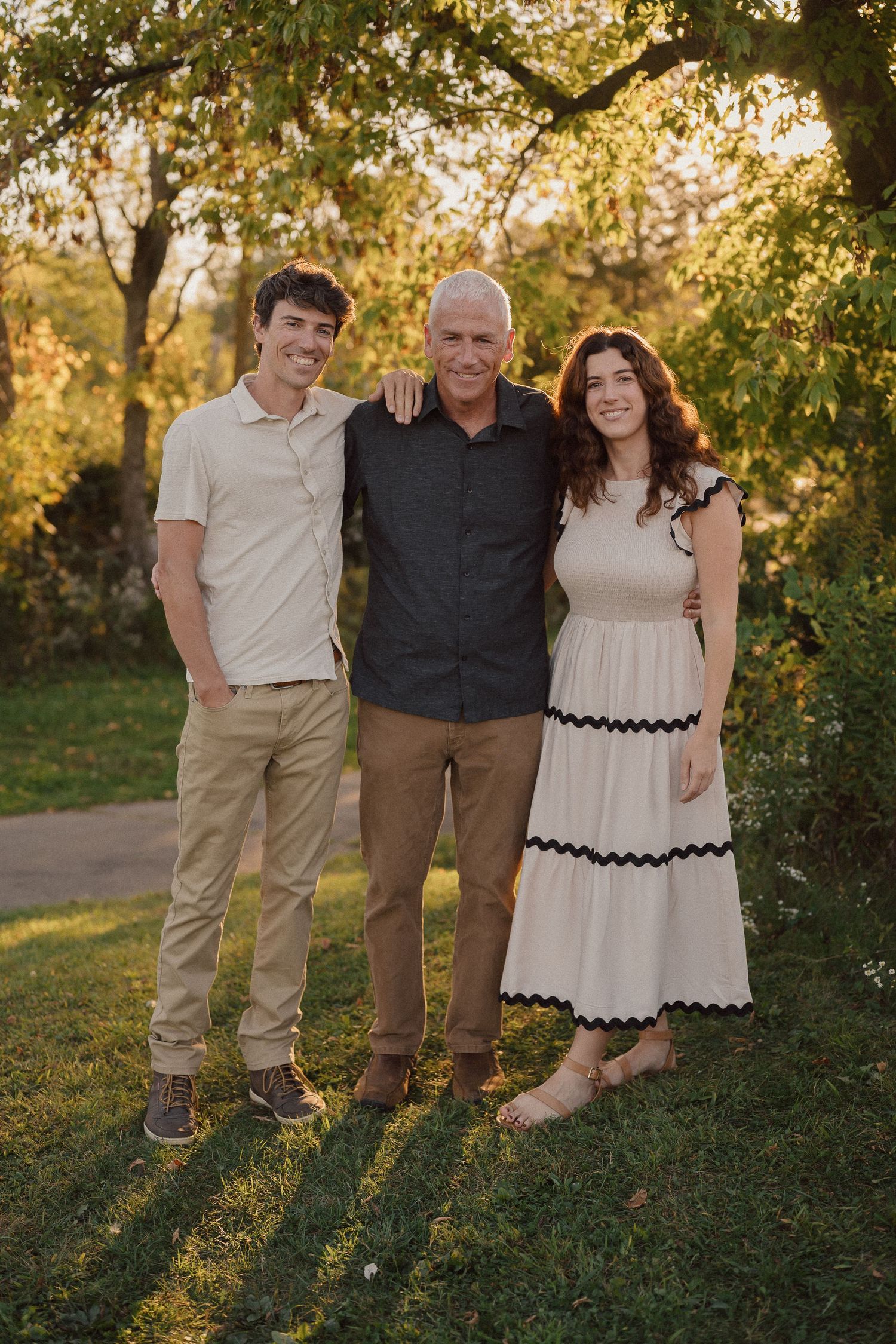 Family portrait in coordinated neutral outfits against trees during golden hour.