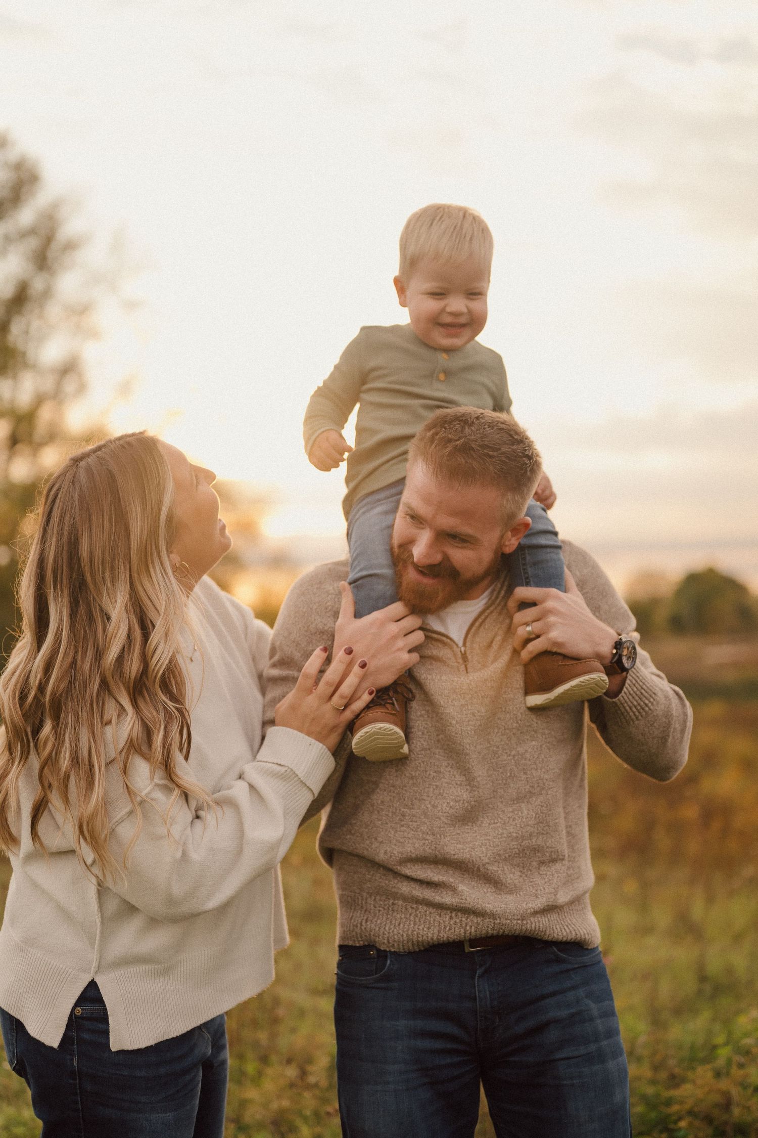 A joyful moment captured as a child rides on shoulders during golden hour in a field.