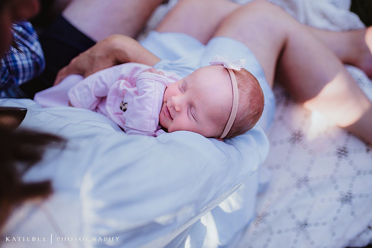 Sleeping newborn in pink with delicate headband rests peacefully on soft fabric.