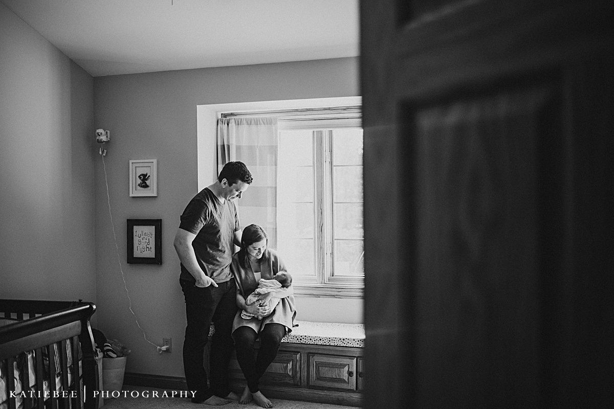 Black and white candid family moment by window in nursery.