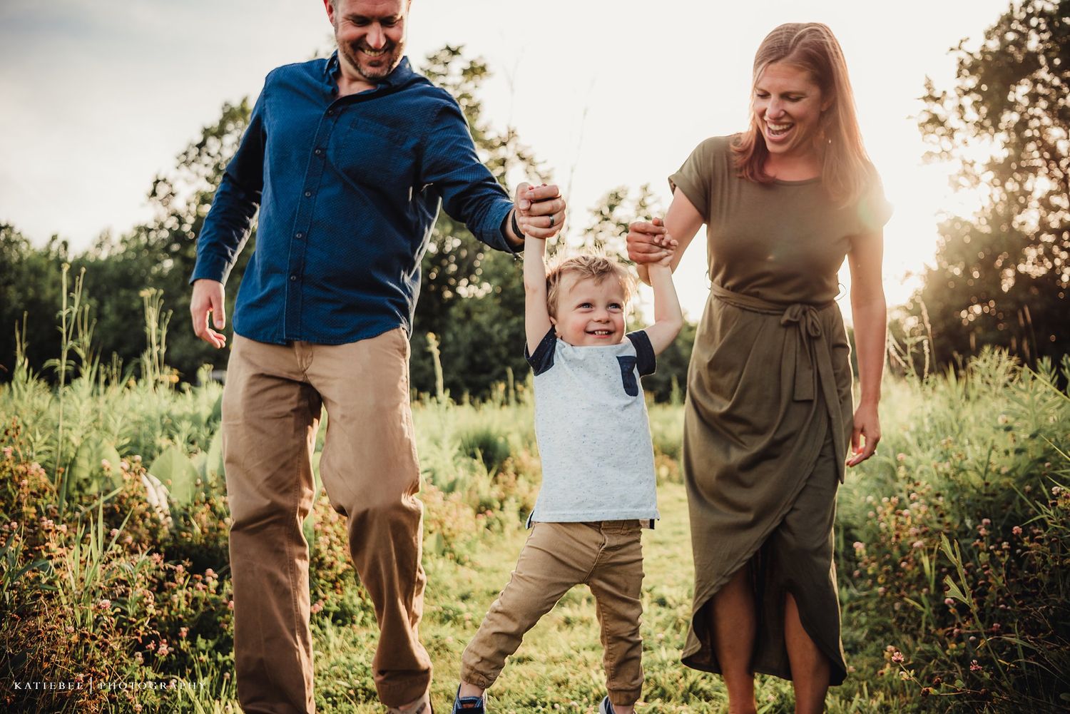 Parents swing their young child between them in a joyful outdoor moment.