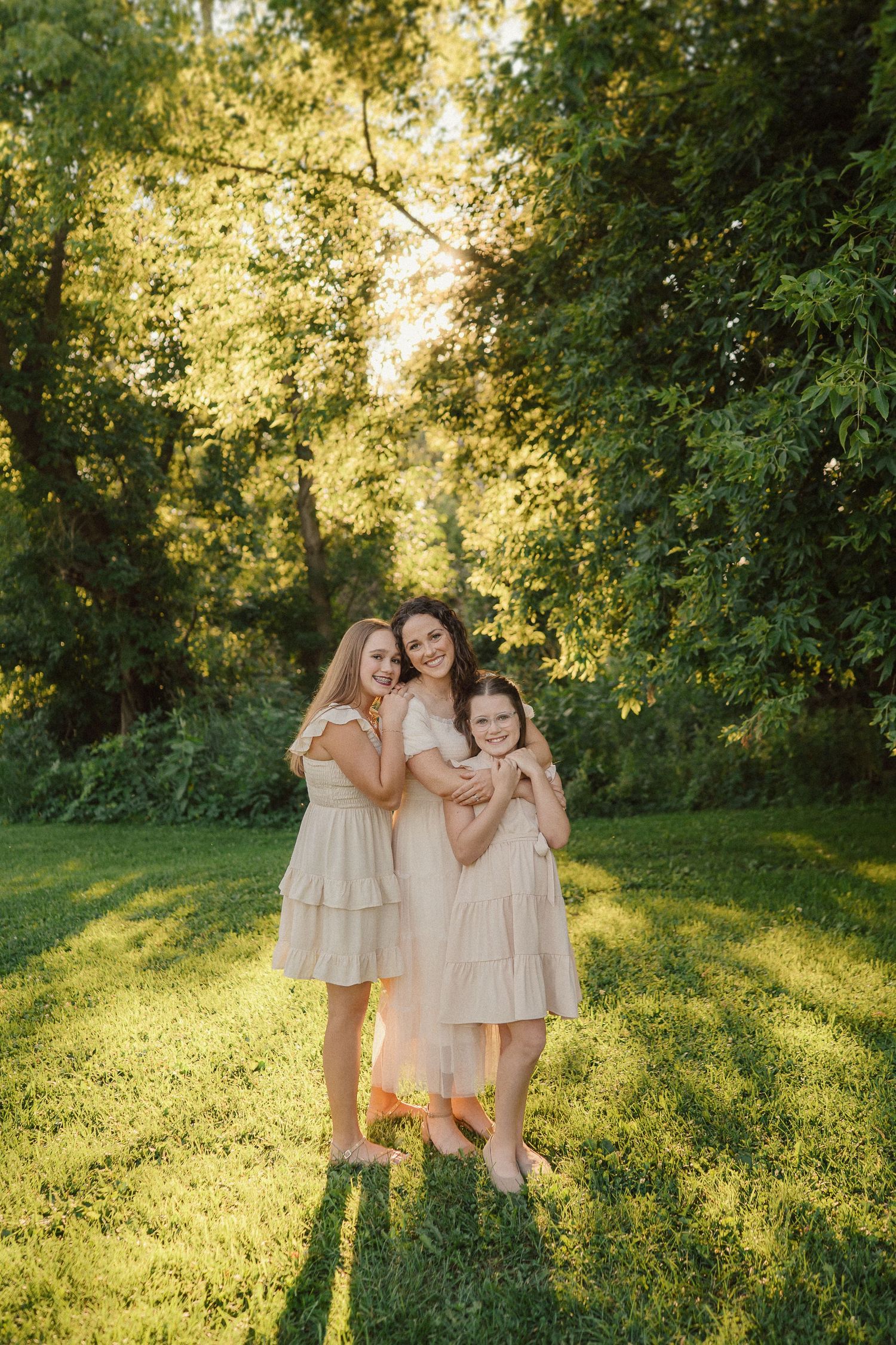 A joyful group shares tender moments together while wearing matching light dresses in a sunlit outdoor setting.