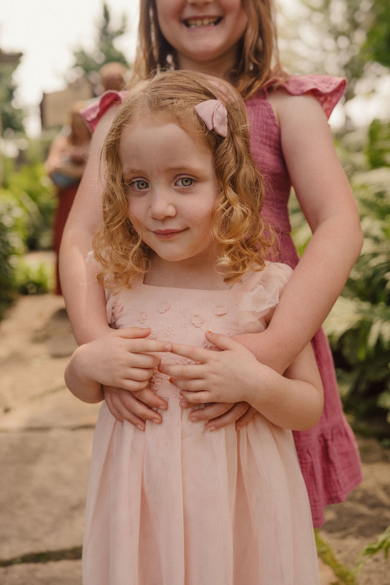 Loving family moments shared in a garden setting with soft pink dresses and gentle gestures.