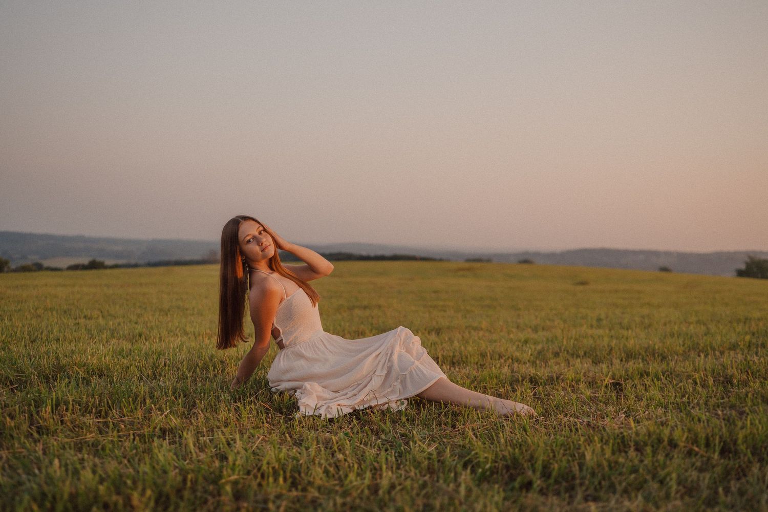 A woman in a white dress lounges serenely across a golden wheat field at sunset.