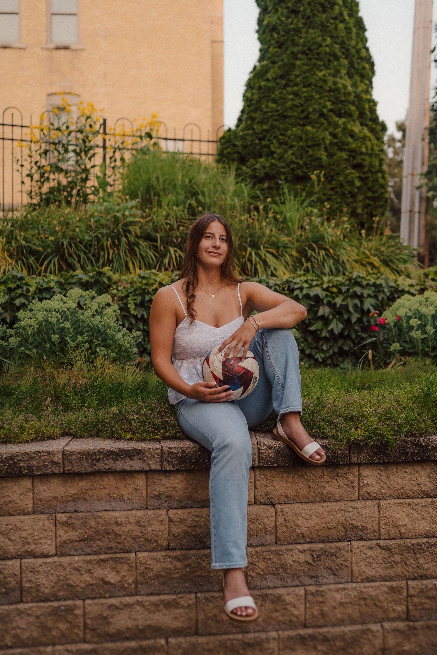 Casual outdoor photoshoot with person sitting on stone retaining wall near garden.