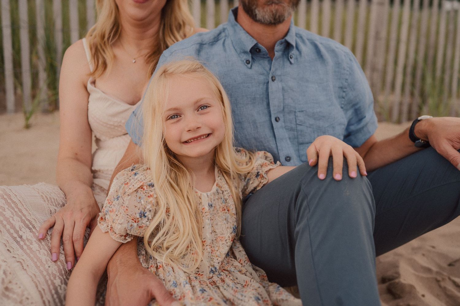 A family sitting together outdoors on a sandy beach with golden lighting at sunset.