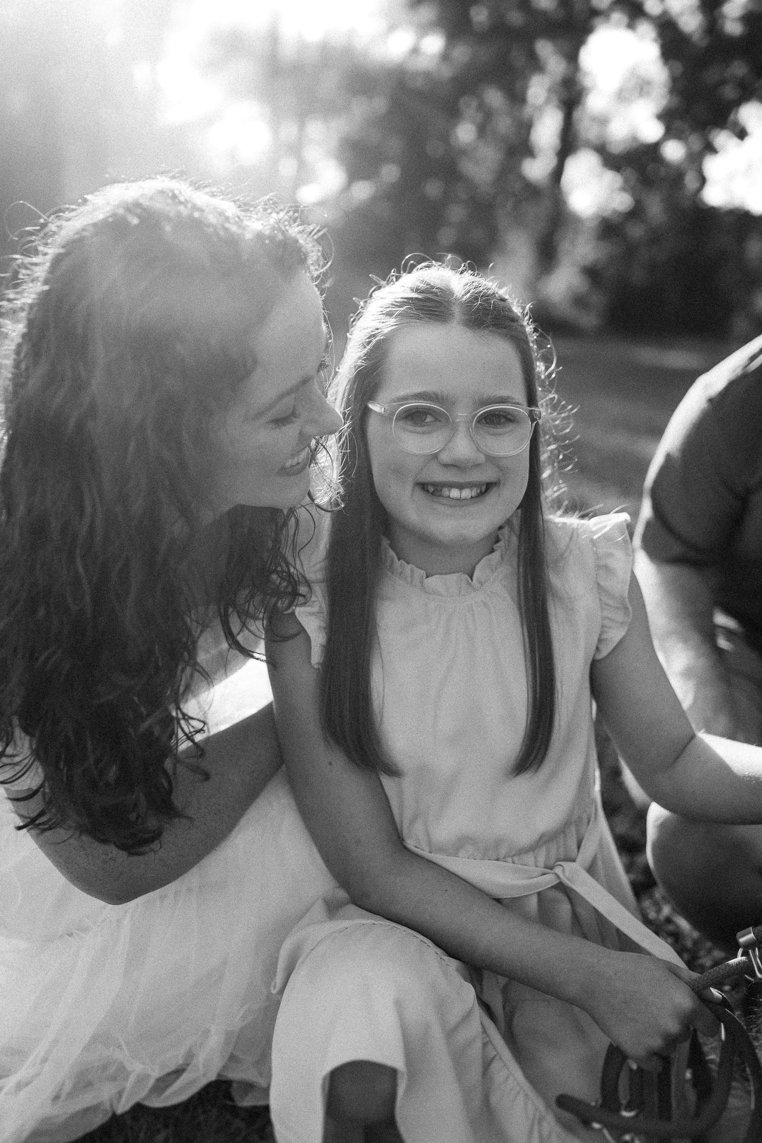 Black and white portrait of a joyful outdoor scene with sunlight filtering through trees in the background.