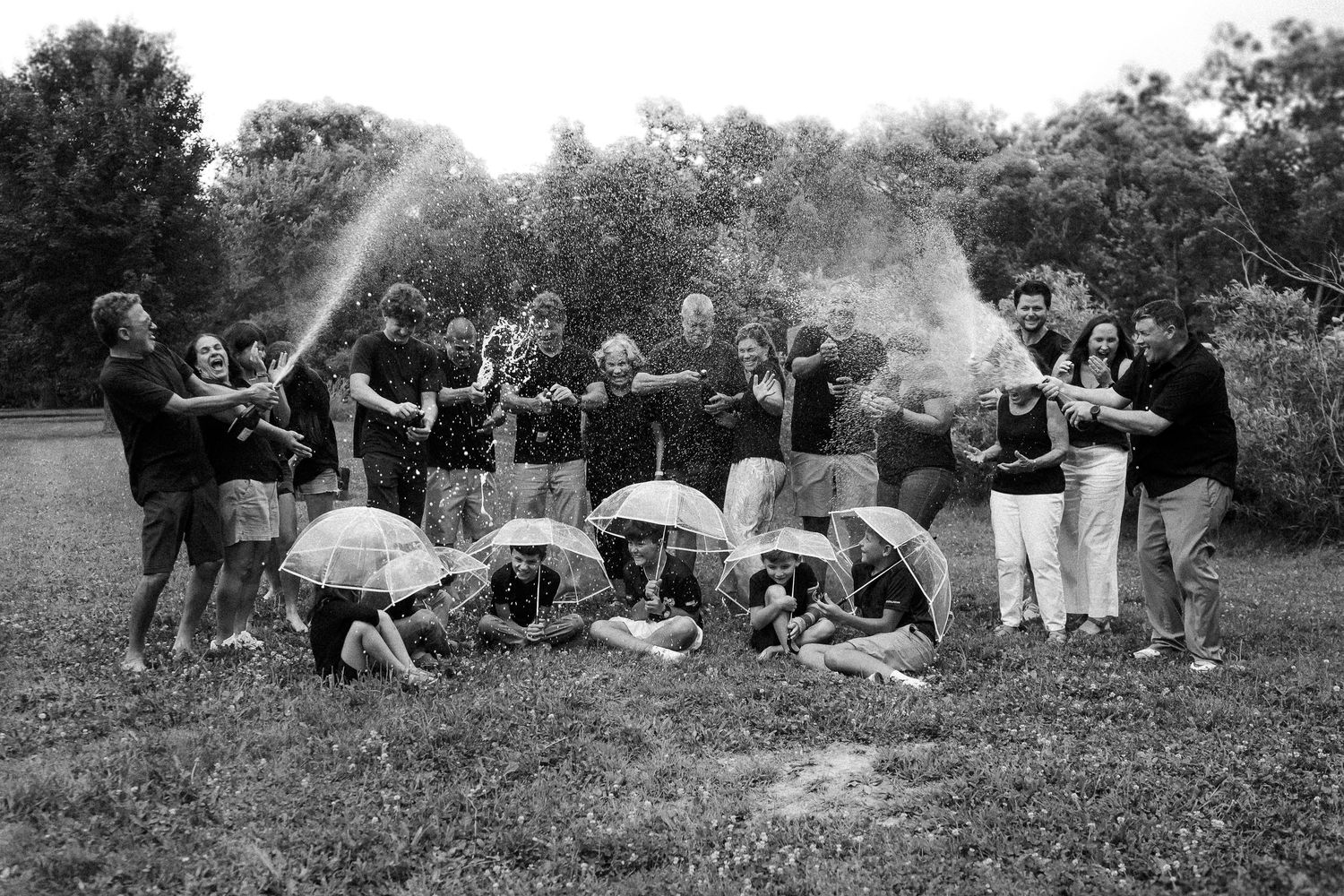 A black and white photograph shows a large group lounging on grass during an outdoor gathering.